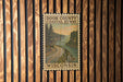 A framed poster of a coastal road in Wisconsin, with a scenic landscape of trees, water, and a winding road.