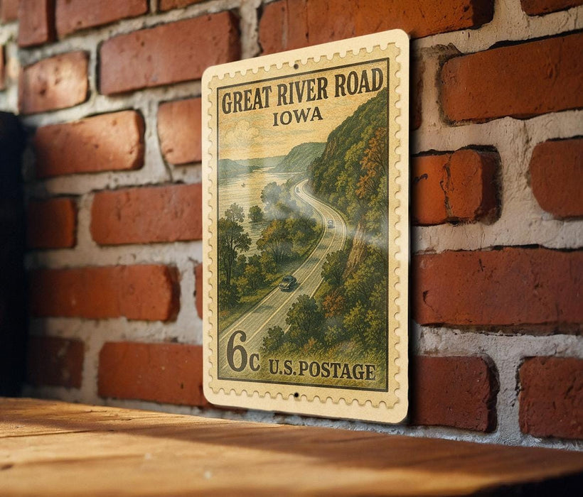 A vintage postage stamp depicting a scenic road in Iowa, mounted on a brick wall.