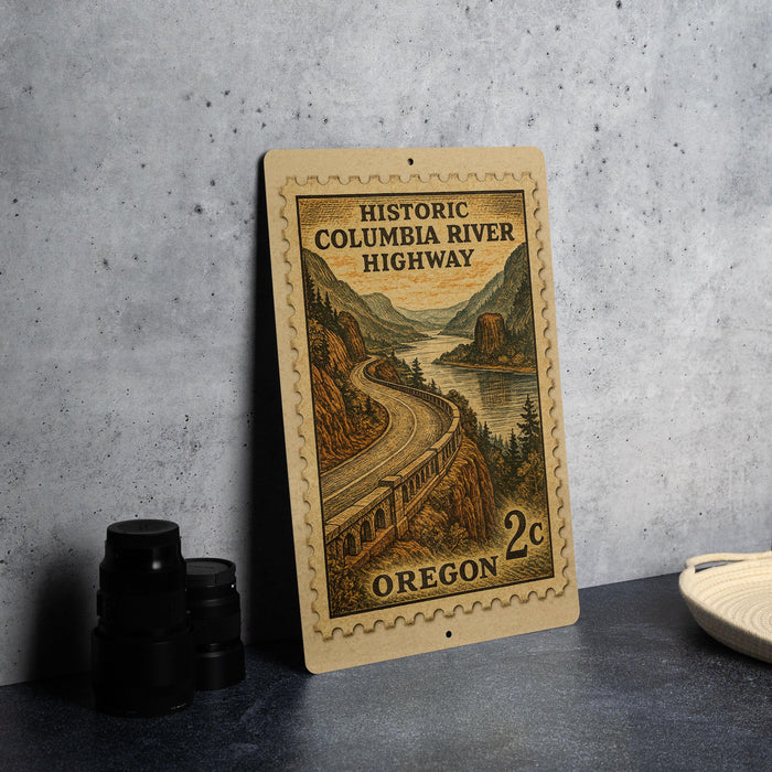 A wooden postcard featuring an illustration of the Historic Columbia River Highway in Oregon, with a mountain landscape and a winding road.