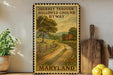A framed poster of a rural road in Maryland, with a wooden fence and a house in the background, is displayed on a shelf next to a wooden cutting board and a potted plant.
