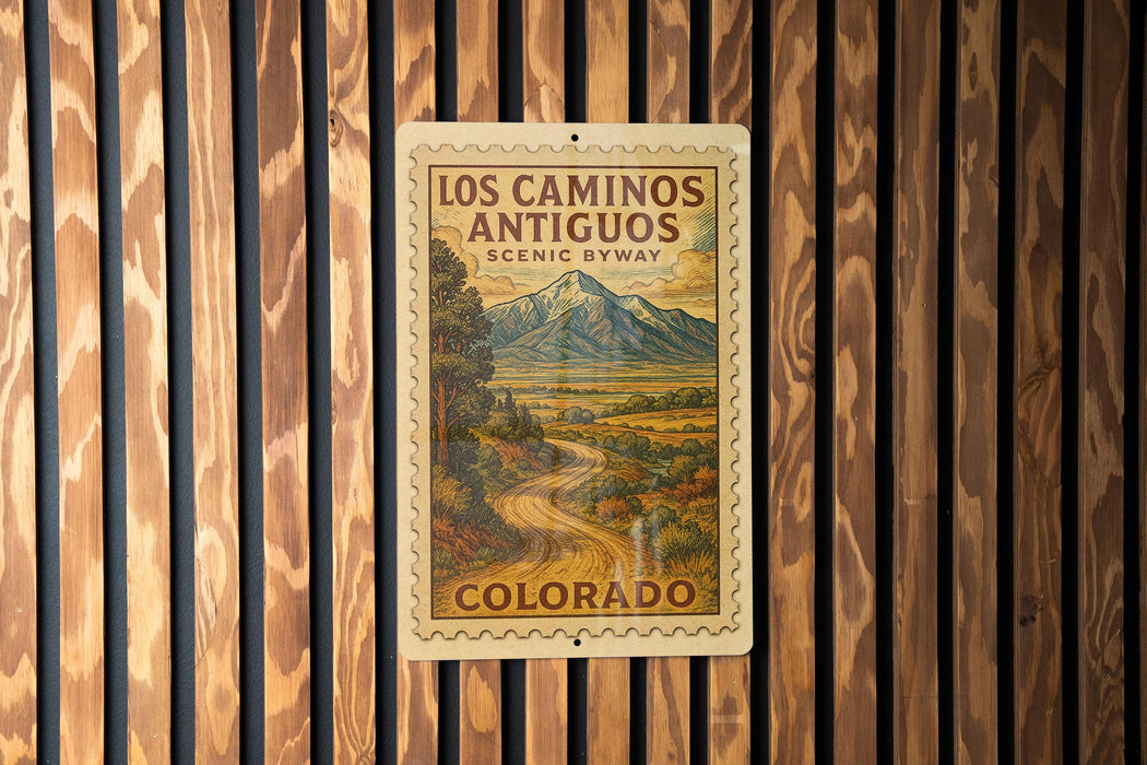 A vintage-style metal sign with a mountain landscape and a road, mounted on a wooden wall.