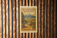 A vintage-style metal sign with a mountain landscape and a road, mounted on a wooden wall.