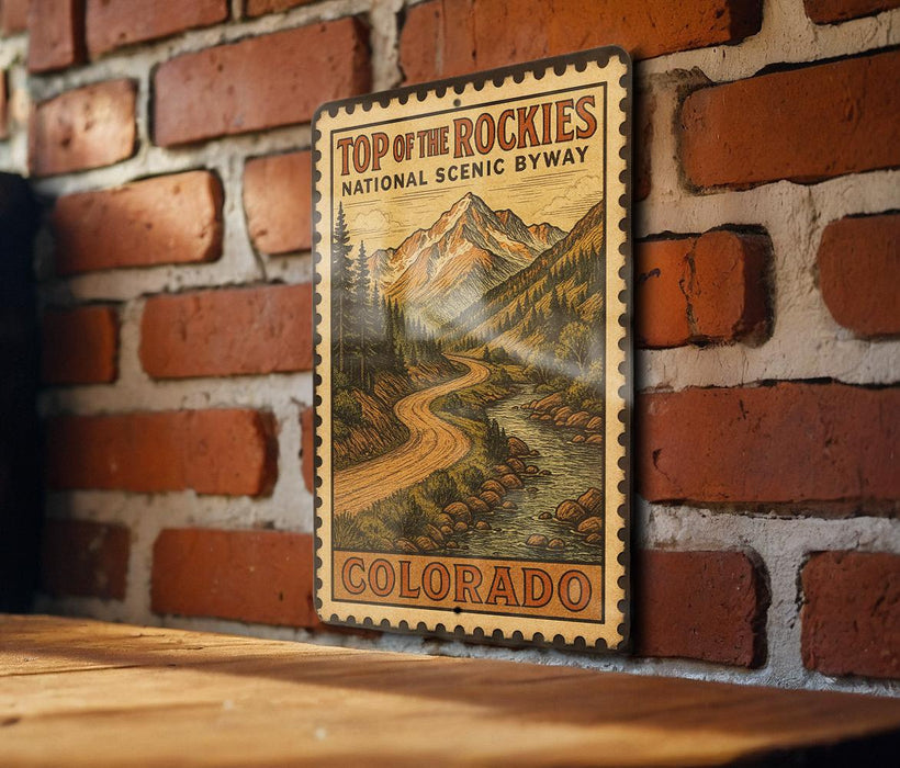 A vintage-style sign for the Top of the Rockies National Scenic Byway in Colorado, featuring a mountain landscape with a winding road and pine trees.