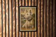 A bull terrier dog is depicted on a postage stamp, which is mounted on a wooden wall.