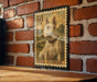 A bull terrier dog is depicted on a postage stamp-like frame, mounted on a brick wall.