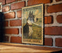A vintage postage stamp featuring a Great Dane dog, mounted on a brick wall.
