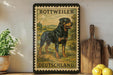 a vintage-style stamp or poster of a Rottweiler dog, with the text "ROTTWEILER DEUTSCHLAND" printed on it. The poster is displayed on a shelf, surrounded by various kitchen items such as a cutting board, a knife, and a bowl.