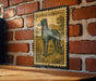 A metal sign with a picture of a Scottish deerhound dog on it, mounted on a brick wall.
