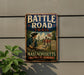 A vintage metal sign on a wall, depicting a historical scene of soldiers on a trail, with the text "BATTLE ROAD TRAIL" and "MASSACHUSETTS" prominently displayed.