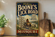 A vintage-style sign for "Boone's Lick Road" in Missouri, featuring a wagon and a signpost with directions to various locations.