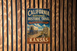 A vintage-style metal sign for the California National Historic Trail in Kansas, featuring an illustration of a covered wagon and a marker for the trail.