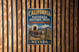 A vintage-style metal sign for the California National Historic Trail, featuring an illustration of a wagon and a sign for Nevada, is displayed on a wooden wall.