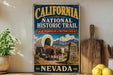 a vintage-style sign for the California National Historic Trail, with a wagon train and mountains in the background. The sign is displayed on a shelf next to a wooden cutting board and a potted plant.