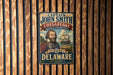 A vintage-style metal sign featuring a portrait of a bearded man, with text indicating that it is from the Chesapeake National Historic Trail in Delaware.