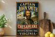 A vintage-style metal sign featuring a portrait of a bearded man, with text that reads "CAPTAIN JOHN SMITH" and "CHESAPEAKE NATIONAL HISTORIC TRAIL VIRGINIA".
