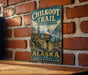 A vintage-style metal sign for the Chilkoot Trail Historic Corridor in Alaska, featuring a hiker and mountainous scenery.