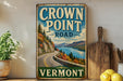 A vintage-style sign for the Crown Point Road in Vermont, featuring a scenic mountain landscape with a winding road and a lake.