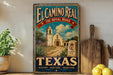 A vintage-style sign for El Camino Real, the Royal Road in Texas, featuring a painting of a historic building and a road leading to it.