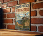 A vintage-style metal sign for the Grand Portage Heritage Trail in Minnesota, featuring a canoe and a castle, is displayed on a brick wall.