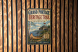 A vintage-style metal sign for the Grand Portage Heritage Trail in Minnesota, featuring an illustration of a canoe and a cabin in a scenic landscape.