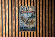 A vintage-style metal sign for the Iditarod National Historic Trail in Alaska, featuring a sled dog team and the text "Iditarod National Historic Trail" and "Alaska".