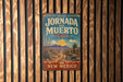 A vintage-style metal sign for the Jornada del Muerto Trail in New Mexico, featuring a desert landscape with mountains and a cactus in the background.