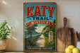 A vintage-style metal sign for the Katy Trail in Missouri, featuring a bicycle and a scenic landscape.