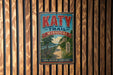 A vintage-style metal sign for the Katy Trail in Missouri, featuring a scenic illustration of a path surrounded by nature.