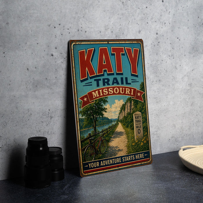 A vintage-style metal sign for the Katy Trail in Missouri, featuring a bicycle and a scenic landscape.