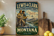 A vintage-style metal sign for the Lewis & Clark National Historic Trail, featuring two men on a mountain trail with a scenic landscape in the background.
