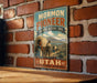 A vintage-style sign for the Mormon Pioneer National Historic Trail in Utah, featuring an illustration of a wagon train and mountains in the background.