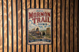 A vintage-style metal sign for the historic Mormon Trail in Iowa, featuring an illustration of a wagon train and a sign with the text "Faith, Courage, Pioneer Spirit" and "Est. 1846".