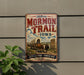 A vintage-style sign for the historic Mormon Trail in Iowa, featuring an illustration of a wagon train and a monument.