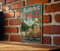 A vintage-style metal sign with the text "NATCHEZ TRACE ALABAMA" and a scenic illustration of a road leading through a forest.