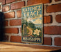 A vintage-style metal sign for the Natchez Trace National Historic Trail, featuring a scenic illustration of a trail surrounded by nature and a large white flower.