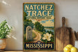 A vintage-style metal sign for the Natchez Trace National Historic Trail, featuring a scenic illustration of a trail surrounded by nature and a prominent signpost.