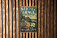 A vintage-style metal sign for the Natchéz Trace National Historic Trail in Mississippi, featuring a scenic illustration of a trail surrounded by nature.
