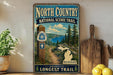 A vintage-style metal sign for the North Country National Scenic Trail, featuring a scenic landscape with pine trees, a lake, and mountains.