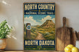 A vintage-style metal sign for the North Country National Scenic Trail in North Dakota, featuring a scenic landscape with mountains and a trail.