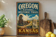 A vintage-style metal sign for the Oregon National Historic Trail in Kansas, featuring an illustration of a covered wagon and a sign that reads "Oregon National Historic Trail Kansas".