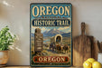 a vintage-style sign for the Oregon National Historic Trail, depicting a wagon train traveling through a scenic landscape with mountains in the background.
