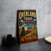 A vintage-style sign advertising the "Overland Trail" in Wyoming, featuring a wagon train and a scenic mountain landscape.