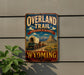 A vintage-style metal sign advertising the "Overland Trail" in Wyoming, featuring a wagon train and a mountain landscape.