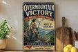 a vintage-style metal sign with a historical illustration of a group of people on a mountain trail, along with text that reads "Overmountain Victory National Historic Trail" and "Follow the path of courage". The sign is displayed on a wooden shelf, with a potted plant and a cutting board visible in the background.