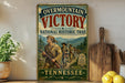 a vintage-style metal sign with the text "Overmountain Victory National Historic Trail" and "Tennessee" printed on it, along with a depiction of a group of people in historical attire. The sign is displayed on a shelf next to a wooden cutting board and a potted plant.