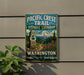 A metal sign on a wall that reads "Pacific Crest Trail Historic Corridor Washington" with a mountain and trees in the background.
