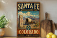 A vintage-style metal sign for Santa Fe National Historic Trail in Colorado, featuring a wagon train and mountains in the background.