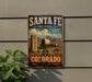 A vintage-style metal sign for the Santa Fe National Historic Trail in Colorado, featuring a wagon train and mountains in the background.