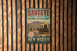 A vintage-style metal sign for the Santa Fe National Historic Trail in New Mexico, featuring a wagon train and a scenic desert landscape.