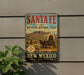 A vintage-style sign for the Santa Fe National Historic Trail in New Mexico, featuring a wagon train and a desert landscape.